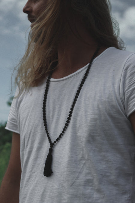 Man in a white t-shirt wearing a Black Onyx crystal mala necklace with a black tassel