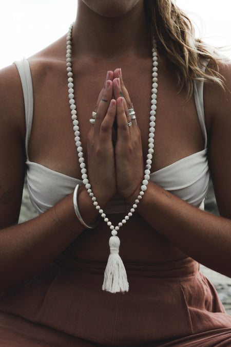 Woman sitting in meditation wearing a long white Howlite beaded and hand knotted mala necklace with a white vintage tassel